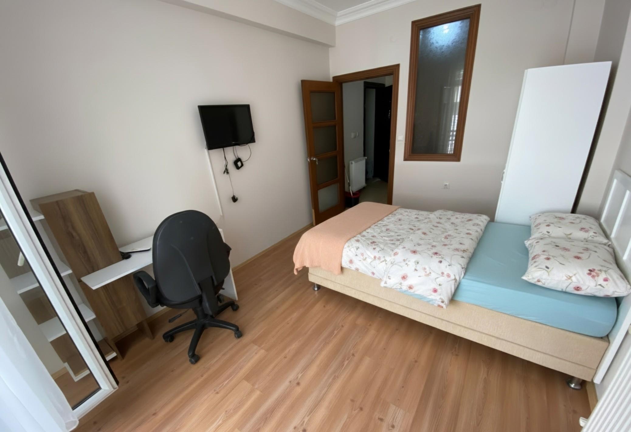 Tek kişilik oda, aydınlık pencere ve çalışma köşesi